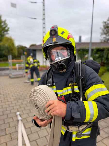 Feuerwehrmann mit Atemschutzmaske und Helm hält Schlauchrolle in Österreich